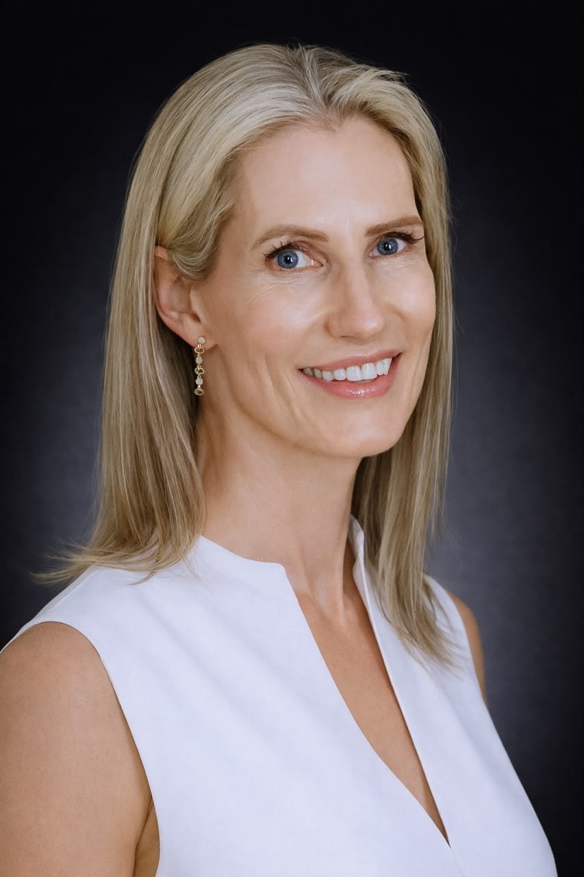 Dr Marisa Venter, smiling, photographed against a dark grey backdrop in a sleeveless white top with drop earrings.